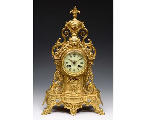 A FRENCH GILT METAL MANTEL CLOCK of ornate scroll form with lion mask decoration and white enamel dial with Roman numerals an
