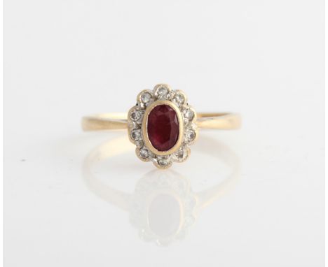 A hallmarked 9ct yellow gold diamond and ruby cluster ring, set with a central oval cut ruby surrounded by a border of ten di