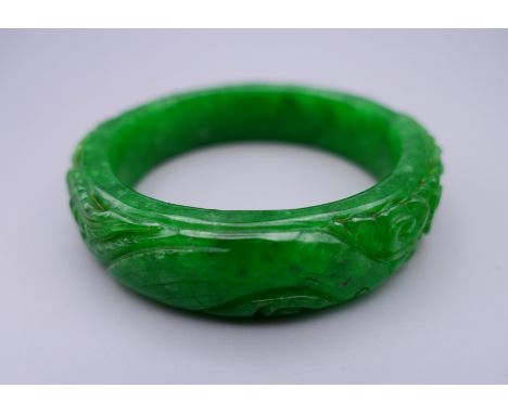 A carved apple green jade bangle. 7 cm diameter.