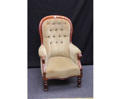 A Victorian mahogany spoon back fireside easy arm chair, with button upholstery, raised on turned fore supports