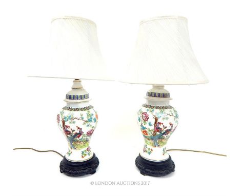 A pair of Chinese style ceramic table lamps with shades, the lamps decorated with peacocks amongst foliage on wood style base