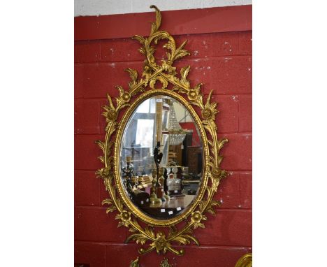 An oval wall mirror, giltwood gadrooned border with carved scrolling foliage and flora, bevel edge glass. 78cm x 54c (153cm x