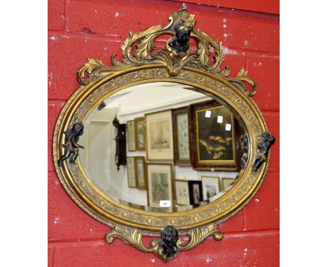 An oval wall mirror, bevel edge glass, the gilt frame carved with flora in relief, maiden's head surrounded by leafy foliage 