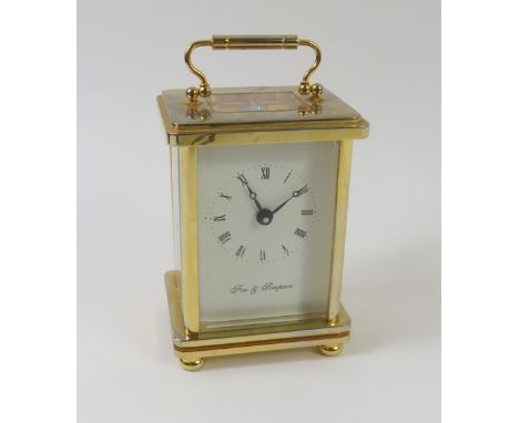 A gold-coloured carriage clock with swing handle at top. Sides, top and rear feature glass allowing for clockwork to be visib