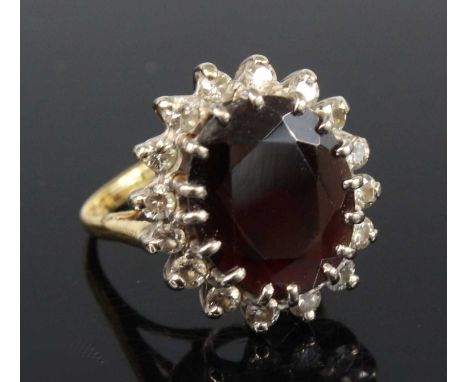 A yellow and white metal, garnet and diamond oval cluster ring, featuring a centre almandine garnet within a border of 16 rou