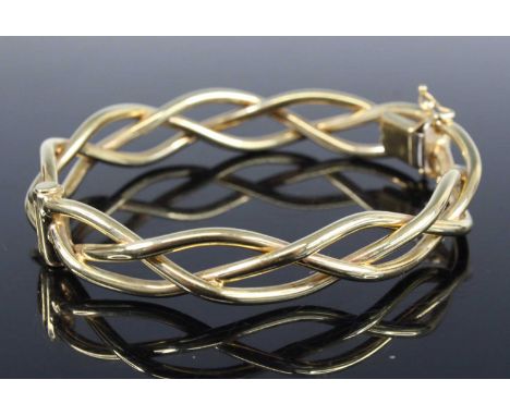 A contemporary 9ct gold hinge bangle arranged as three interwoven bands, with safety chain, 18.9g, dia. 7cm