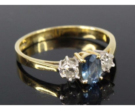 An 18ct yellow and white gold, sapphire and diamond three-stone ring, featuring a centre oval sapphire flanked on either side
