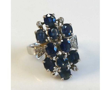 A white metal sapphire and diamond abstract cluster ring comprising 10 oval facetted sapphires in tiered claw settings with a