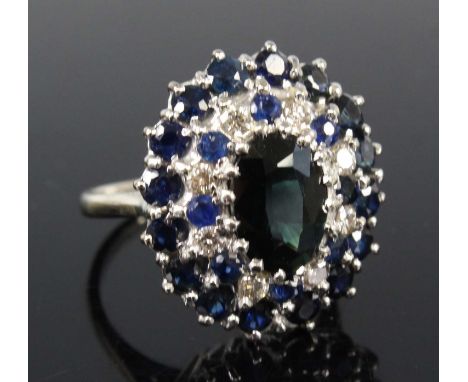 An 18ct white gold, sapphire and diamond oval cluster ring, featuring a centre oval sapphire within a border of eight round b