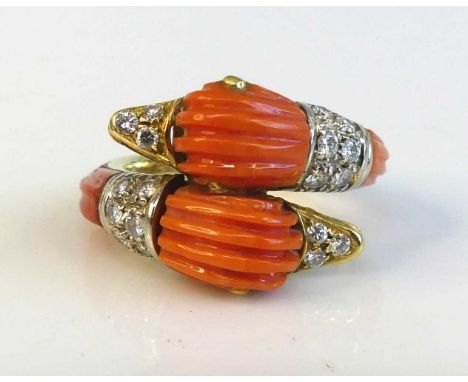 A yellow metal and coral and diamond twin duck head crossover style ring featuring carved coral detail to the heads and shoul