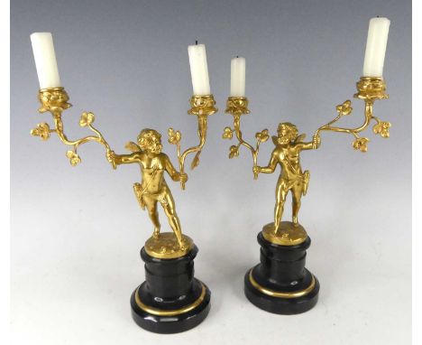 A pair of French circa 1900 gilt bronze figural candelabra, each modelled as a standing winged putti holding branches with sc