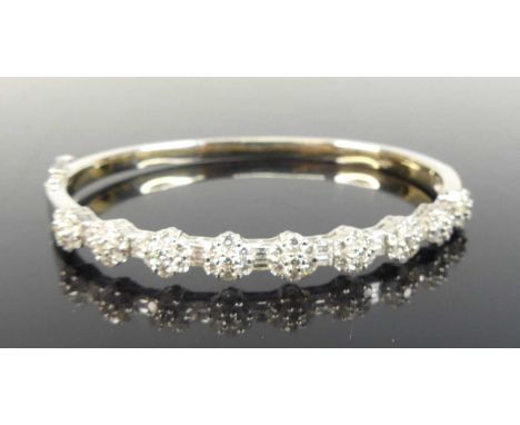A white metal diamond oval hinged bangle, featuring nine circular clusters each with seven round brilliant cut diamonds alter