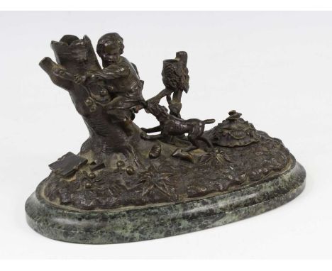 A circa 1900 bronze inkstand, of oval form, featuring a boy escaping a playful dog, the whole raised upon a verdigris marble 