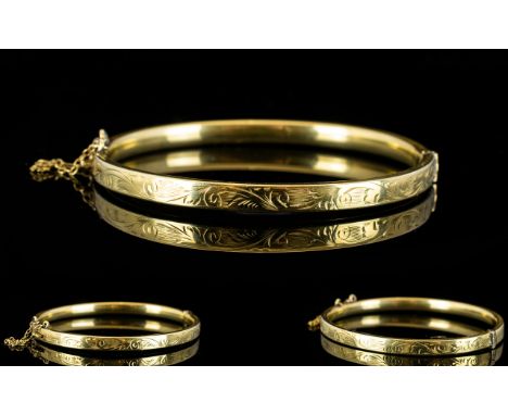 A 9ct Gold Hinged Bangle with Safety Chain, Stylised Floral Decoration to Outer Side of Bangle. c.Early Part of 20th Century,