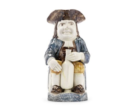 A very rare Prattware 'Bottle' Toby Jug, circa 1800Modelled seated and with a lop-sided stare, holding a long square bottle b