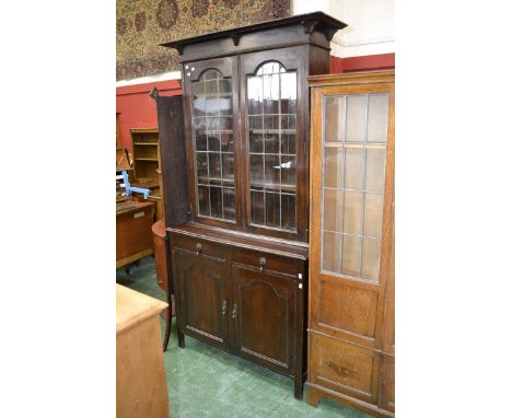 An oak bookcase cabinet, outswept cornice, two lead glazed doors enclosing shelving to top, projecting base, two short drawer