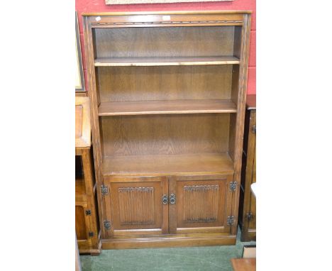 An Old Charm oak bookcase cabinet, shelving to top over pair of cupboard doors enclosing shelving to base, linen fold doors