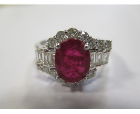 A contemporary ruby and diamond cluster ring, the oval cut ruby claw set between baguette cut diamond shoulders and a crossov