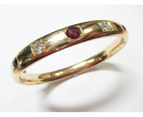 A ruby and diamond hinged bangle, of oval form and hollow oval cross-section, set to the front with three round cut rubies sp