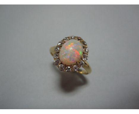 An opal and diamond cluster ring, the oval cabochon opal set in a border of fourteen old European cut diamonds to a plain tap