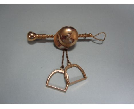 A racing brooch, designed as a jockey's cap on a stylised racing whip suspending a pair of stirrups on short chains, of rose 