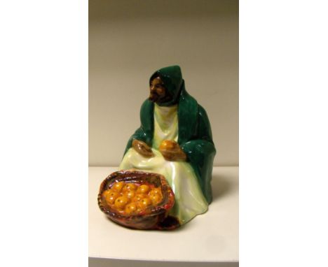 A Royal Doulton figure of an orange seller, HN72, he sits before his basket of oranges wearing a dark green hooded cloak over