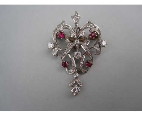 An Edwardian diamond and ruby pendant / brooch, of pierced scrolling form set throughout with single cut diamonds and four ro