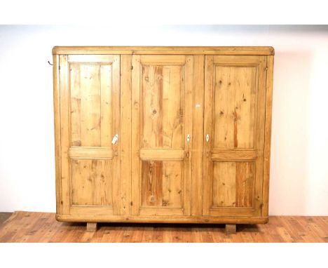 A 20th Century pine triple wardrobe, the three doors opening to reveal a shelf to the top and hanging rail, raised on block s