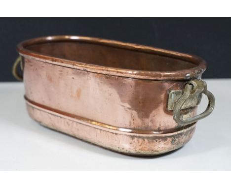 Copper planter of elongated oval form with rolled rim and brass drop loop handles, 33cm long