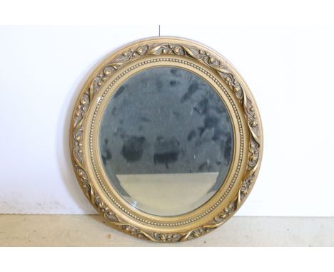 Early 20th century oval gilt framed mirror, the surround chased with flowers and foliage, beaded border withinm with central 