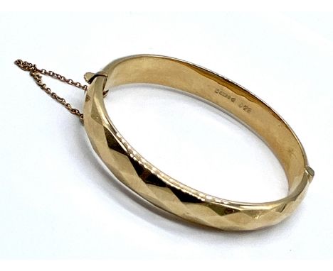 A 9ct gold vintage hinged bangle with fitted safety chain, 12g total weight.