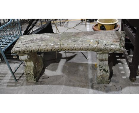 A reconstituted stone curved garden bench on plinths, with cherub detailing - some restoration