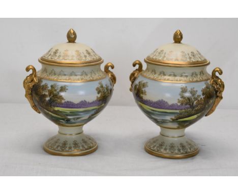 A pair of hand painted lidded twin handled ceramic urns with lake scene with swans and gilded foliate detailing. 