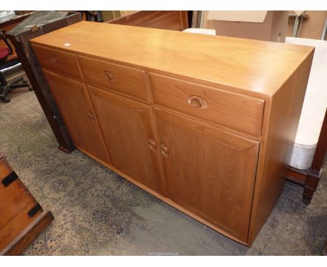 An Ercol Windsor light Elm Sideboard having three frieze drawers and three rotary wooden latched cupboards below, standing on