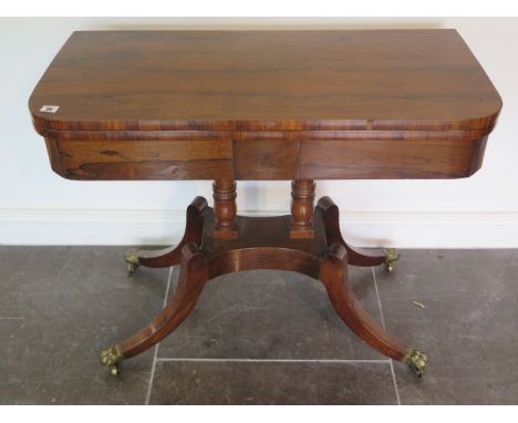 A 19th century rosewood fold over card table on twin turned columns and quatrefoil base terminating on brass claw feet and ca