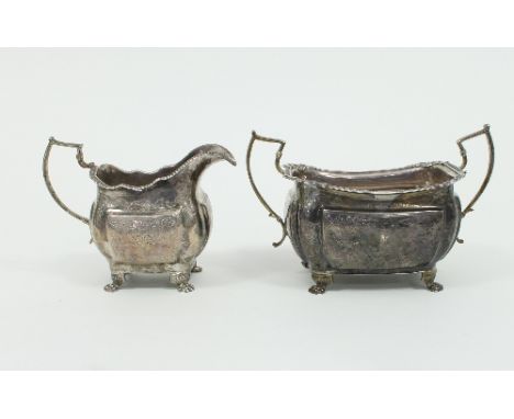An Irish silver sugar basin and cream jug, Dublin circa 1820, each of rectangular shape on paw feet with engraved foliate dec