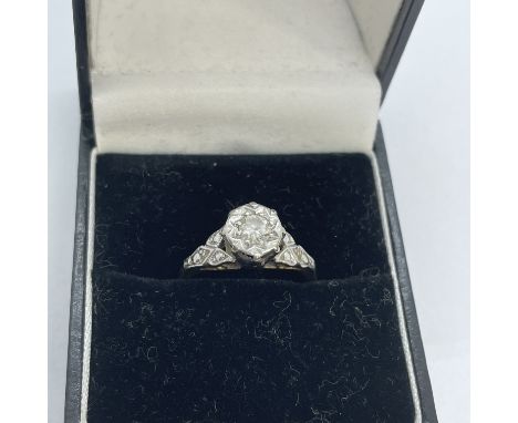 An 18ct gold diamond solitaire ring with a raised foliate white metal setting. The diamond, an estimated 0.20 carat round bri