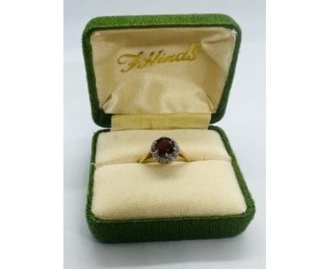 An 18ct almandine garnet and diamond cluster ring. Featuring a central round mixed cut garnet and 12 old cut diamonds. Size L