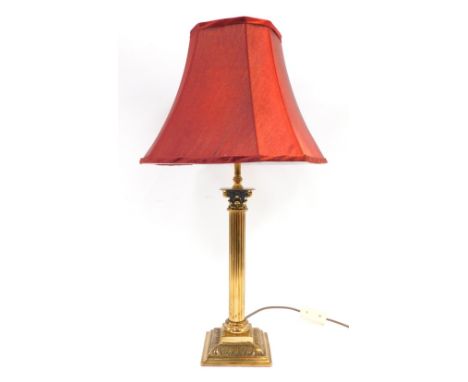 An early 20thC brass Corinthian column lamp base, with reeded supports on a step base with red draylon shade, 61cm high.