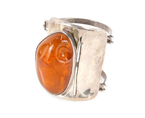 An amber bangle, with abstract design central panel and applied and raised amber piece, with sand type effect illusion bottom