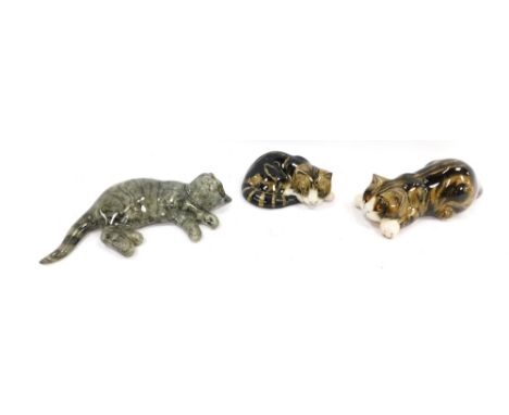 Three Mike Hinton ceramic cats, comprising a grey cat laying down with applied glass eyes, 26cm wide, a brown and black curle
