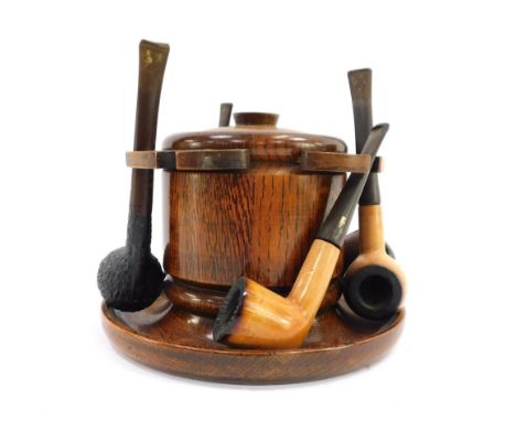 An early 20thC oak smokers stand, with central tobacco jar and with ceramic insert and six piece pipe rack, with five various