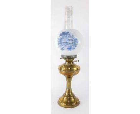A brass oil lamp, with a white shade bearing applied blue detail of cottages, on a stepped brass base with chimney, 65cm high