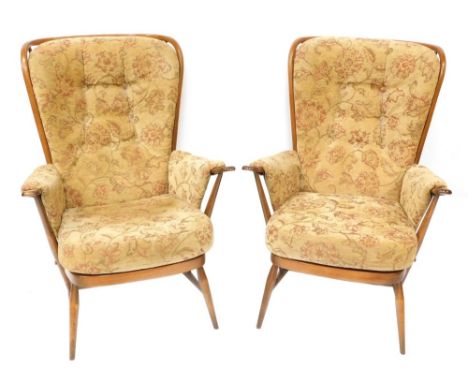A pair of Ercol style upholstered wingback armchairs, each with a light elm finish and applied and buttoned floral upholstery