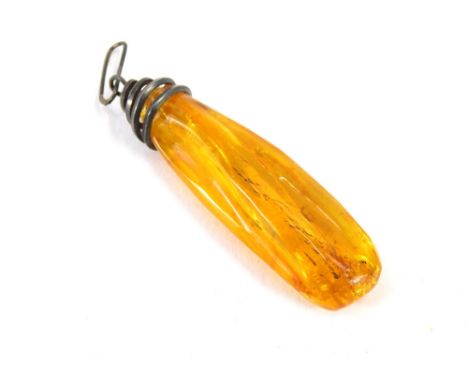 An amber pendant, the polished light orange amber, with outer reeding and a white metal spiral pendant mount with single loop