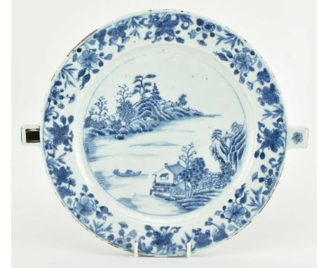 A Qing dynasty blue and white ceramic warming plate. The circular plate decorated with a landscape, river, house, trees and m