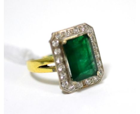 An emerald and diamond cluster ring, the emerald-cut emerald in a white claw setting, within a border of round brilliant cut 