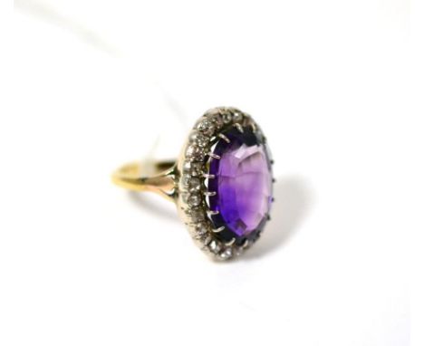 An amethyst and diamond ring, the oval mixed cut amethyst in a white claw setting, within a border of old cut diamonds in rub