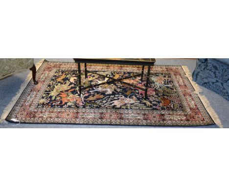 A Ghom silk rug, Central Persia, The indigo field of hunting scene enclosed by coral pink cartouche borders of stylised text,