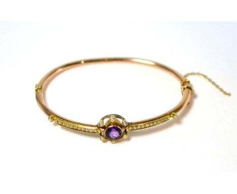 A 9ct gold amethyst and seed pearl bangle, a round cut amethyst in a yellow milled setting within a border of seed pearls and